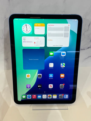 A black Apple iPad Pro with a blue-gray bezel stands upright on a clear acrylic display stand on a white surface, with a marble-patterned background.