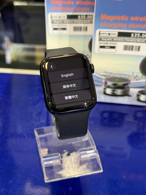 Smartwatch with language selection interface on a blue surface with a magnetic wireless charging stand in the background.
