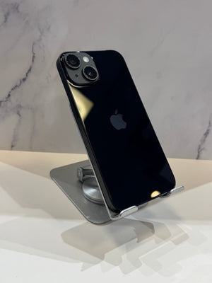 A black Apple iPhone 12 Pro shown from the back, resting on a silver metal stand against a light marble-patterned background.