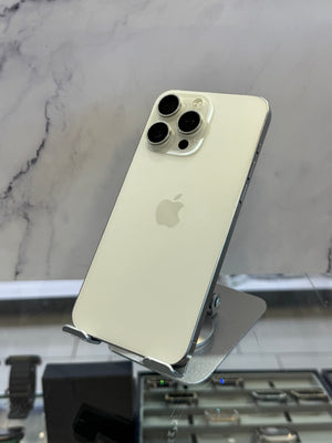 An Apple iPhone in light gold or pale champagne color, shown from the back on a metal display stand in a retail setting with a marble-patterned background.