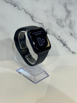 Black Apple Watch with a black band displayed on a clear acrylic stand against a white marble-patterned background.
