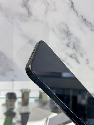 A close-up of a black smartphone corner resting on a white marble-patterned surface, with a blurred display stand in the background.