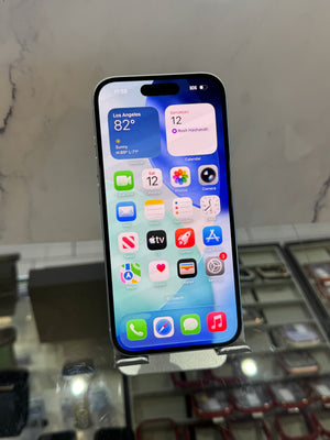 A black Apple iPhone with a silver front bumper and a silver stand, displaying its home screen in a retail store setting.