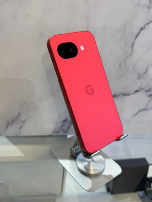 A red Google Pixel smartphone shown from the back, resting on a silver metal display stand against a white marble-patterned background.