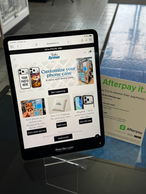 Tablet displaying a phone case customization website on a glass surface with an Afterpay advertisement.