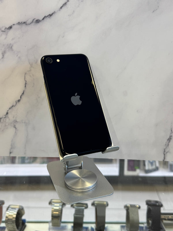 A black Apple iPhone with a silver metallic edge, shown from the back, resting on a white marble-patterned surface next to a silver magnetic display stand.