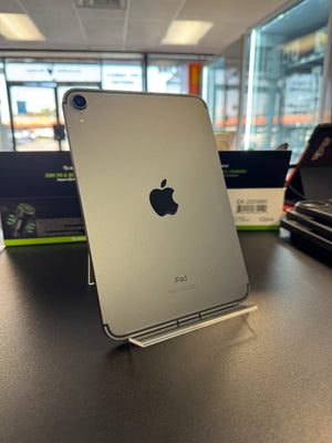 A silver Apple iPad shown from the back, standing on a clear display stand on a dark countertop inside a store.