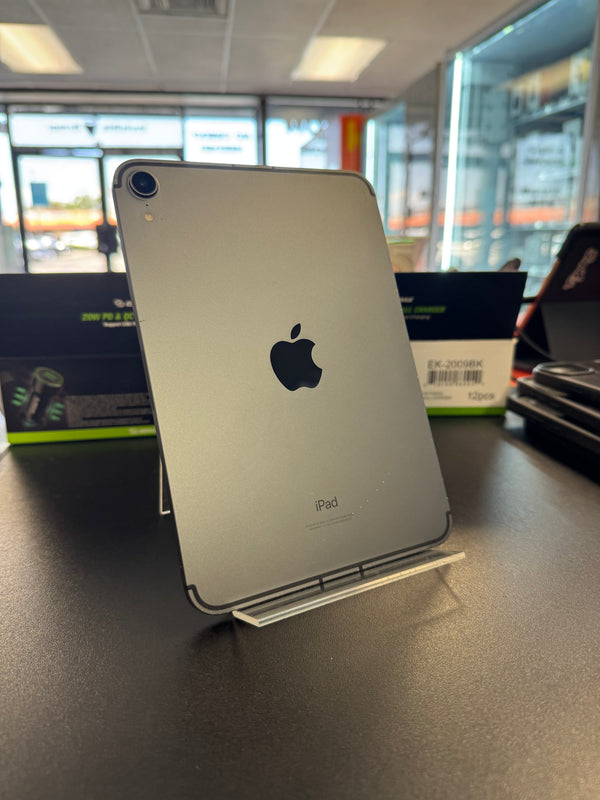 A silver Apple iPad shown from the back, standing on a clear display stand on a dark countertop inside a store.