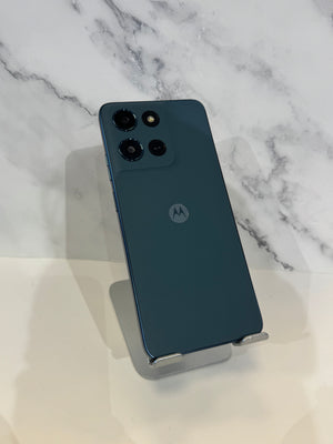 A dark teal-blue Motorola smartphone shown from the back, resting on a small metallic display stand against a white marble-patterned background.