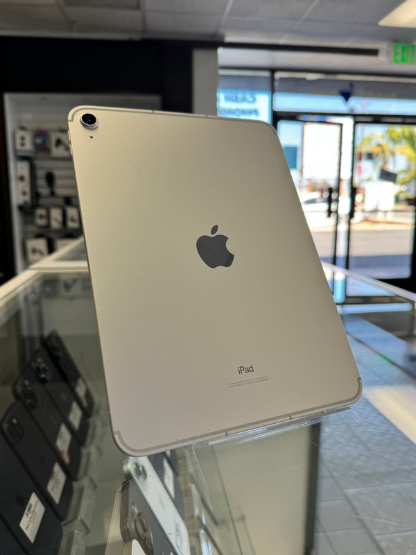 A silver Apple iPad shown from the back, resting on a glass display counter inside a retail store. The Apple logo is clearly visible in the center.