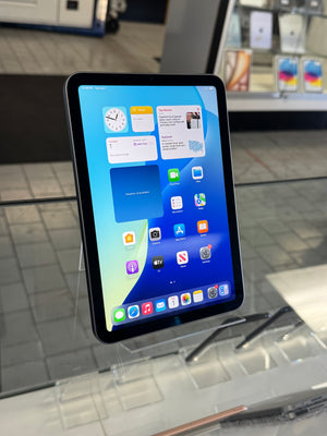 An iPad Pro with a black bezel and a colorful home screen, displayed on a clear acrylic stand in a retail store setting.