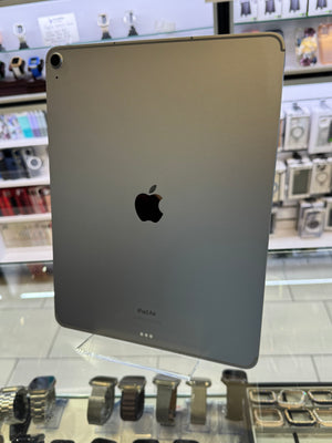 A silver Apple iPad shown from the back, featuring the iconic black Apple logo in the center, photographed inside a retail store with display cases visible in the blurred background.