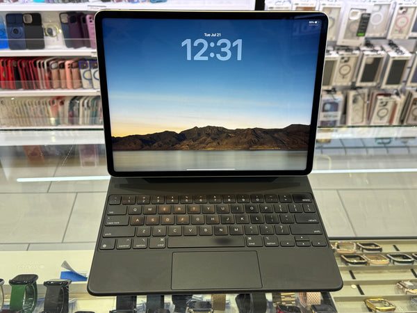 A dark gray Microsoft Surface Laptop with a matching keyboard cover, displayed on a retail counter with a scenic landscape wallpaper on its screen.