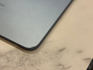 Close-up of the corner of a silver iPad resting on a light marble-patterned surface.
