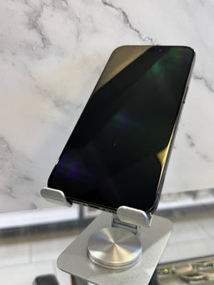 A black smartphone with a glossy screen resting on a silver metal display stand, set against a white marble-patterned background.