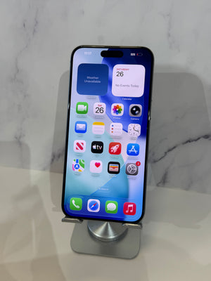 A black iPhone with its home screen on, resting on a silver metal phone stand against a white marble-patterned background.