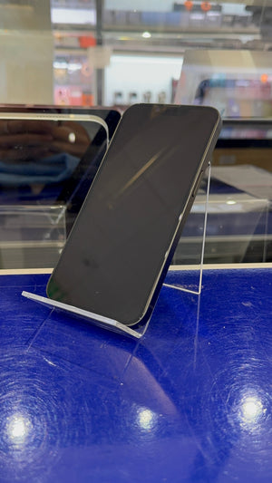 A black smartphone displayed upright on a clear acrylic stand on a glossy blue counter, with a blurred retail store background.