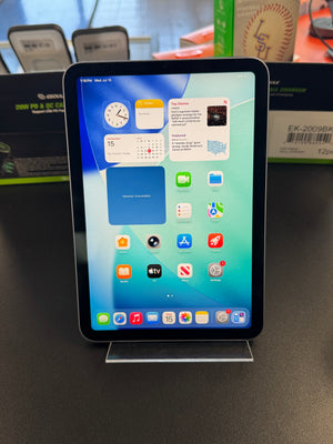 A black Apple iPad tablet with its screen turned on, resting on a dark gray surface next to its original retail packaging.