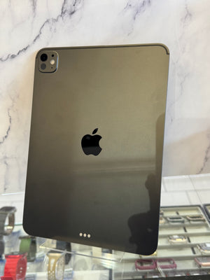 A dark gray Apple iPad shown from the back, resting on a white marble surface with a blurred store background visible on the right.