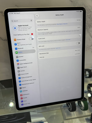 A tablet device displaying the Apple Account battery settings screen, photographed indoors against a light stone or marble wall.