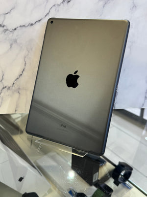 An Apple iPad with a dark metallic gray finish, shown from the back resting on a clear display stand.