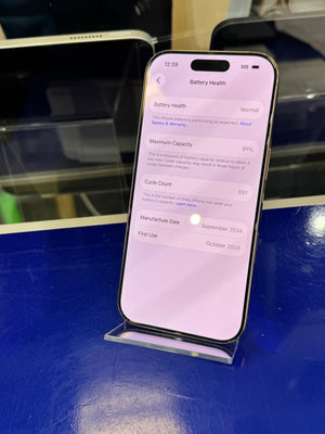 An Apple smartphone displayed upright in a clear stand on a glossy blue surface, with its screen turned on. 