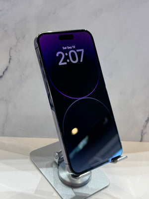 A silver smartphone with a black screen displaying the time 2:07, resting on a metallic stand against a light gray marble-patterned background.