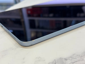 A close-up shot of a tablet's corner showing a light blue-gray aluminum bezel and a black screen, resting on a white marble surface.