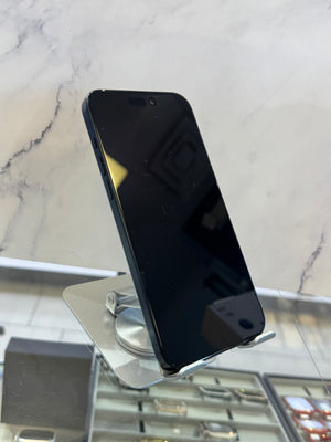 A black smartphone with a large black screen, shown standing upright on a clear display stand in a retail or showroom setting with a marble-patterned background.