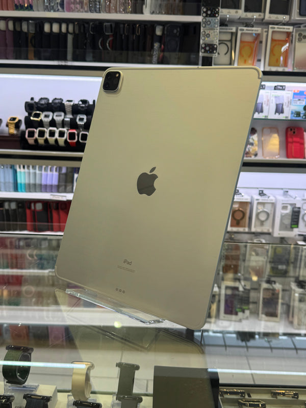 A silver-colored iPad Pro shown from the back, resting on a clear display stand inside a retail store with shelves of accessories in the background.