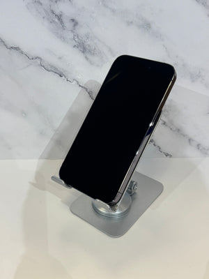 A black smartphone with a silver edge resting on a metallic silver stand, set against a white marble-patterned background.