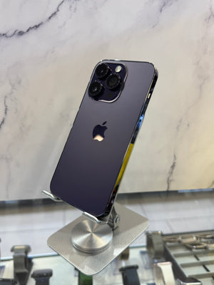 A dark purple Apple iPhone 12 Pro shown from the back, resting on a silver display stand on a white marble-patterned surface.