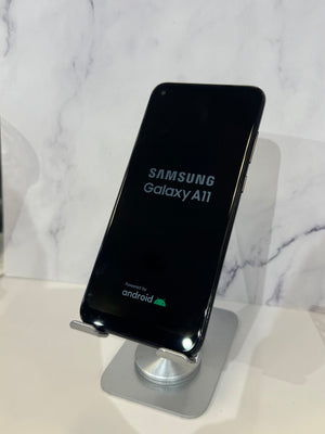 A Samsung Galaxy A11 smartphone displayed upright on a silver stand against a white marble-patterned background.