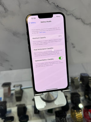 A smartphone on a display stand showing the Battery Health settings screen, photographed in a retail or showroom environment with watches and a marble-patterned wall in the background.