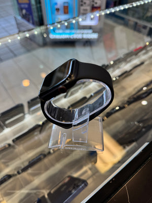 Black smartwatch on a clear stand with a blurred store interior in the background
